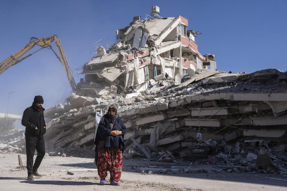 Local residents walk in front of a destroyed building in Nurdagi, southeastern Turkey, Thursday, Feb. 9, 2023. Thousands who lost their homes in a catastrophic earthquake huddled around campfires and clamored for food and water in the bitter cold, three days after the temblor and series of aftershocks hit Turkey and Syria. (AP Photo/Petros Giannakouris)