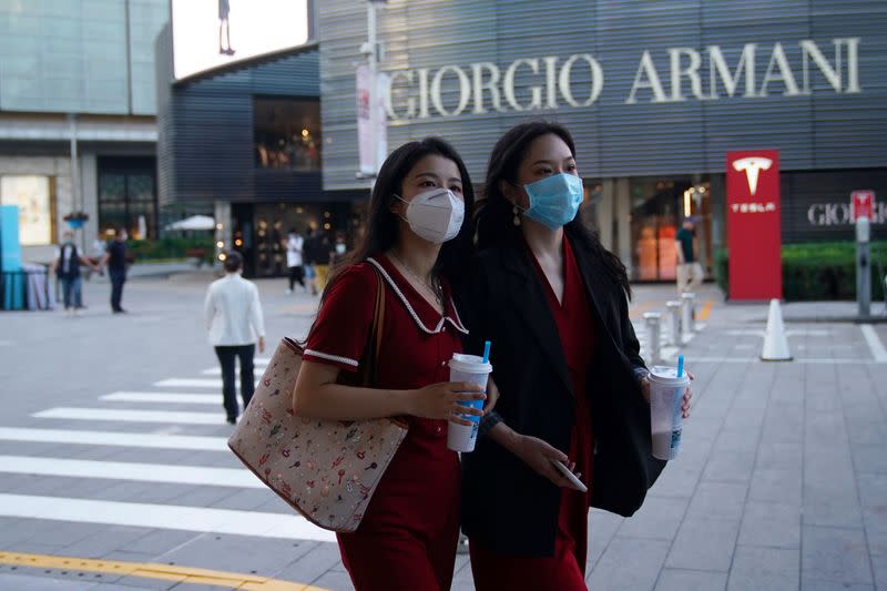 People wearing face masks following the COVID-19 outbreak walk past a store of Italian luxury Giorgio Armani at a shopping complex in Beijing