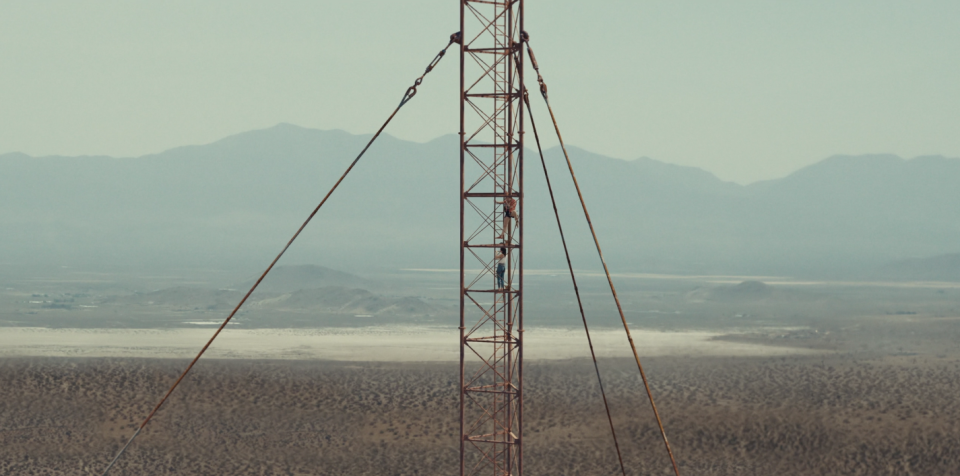 Two girls climb a seemingly endless ladder amidst a desert and mountainous landscape