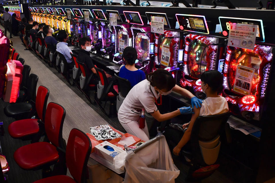A woman receives the first shot of the Moderna COVID-19 vaccine as others wait for their turn in front of pachinko pinball machines at the pachinko parlor Freedom in Osaka, western Japan, Monday, Sept. 13, 2021. A nearby hospital dispatched medical workers to administer the vaccine to 1,500 people in two days at the pinball parlor which became a makeshift vaccination site. (Kyodo News via AP)