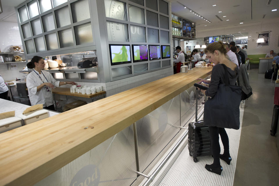 In this Wednesday, Nov. 14, 2012 photo, a guest waits for her food at the Food Network Kitchen at the Fort Lauderdale-Hollywood International Airport, in Fort Lauderdale, Fla. Dining-on-the-go is soaring at the airport where travelers can dine at a restaurant inspired by a test kitchen. The Fort Lauderdale-Hollywood International Airport is the first outpost in the nation to offer the Food Network Kitchen, designed to look much like what you would see in the cable network's test kitchen: a butcher block bar counter, subway tiling, stainless steel surfaces and pots and pans hanging in a row behind a cash register. (AP Photo/J Pat Carter)