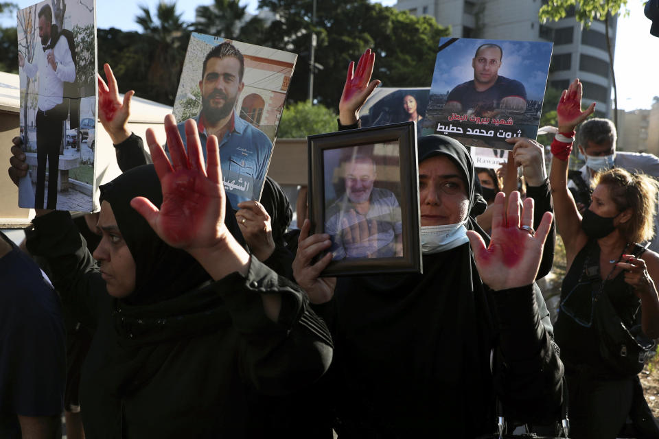 Relatives of people who were killed in last year's massive blast at Beirut's seaport, hold portraits of them as they raise their hands painted red to represent blood, outside the home of caretaker Interior Minister Mohamed Fehmi, in Beirut, Lebanon, Tuesday, July 13, 2021. Family members are angry with Fehmi because he rejected a request by the judge investigating the explosion to question Maj. Gen. Abbas Ibrahim, who is one of Lebanon's most prominent generals and heads of the General Security Directorate. (AP Photo/Bilal Hussein)