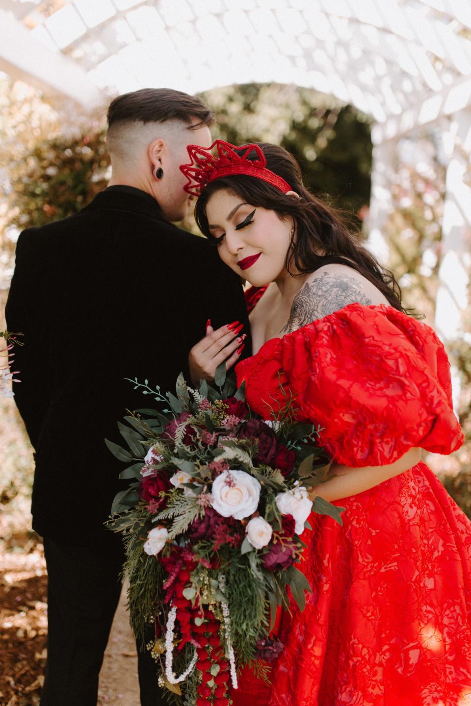 A woman in a red dress leans her head on the shoulder of a man in a black suit and closes her eyes.