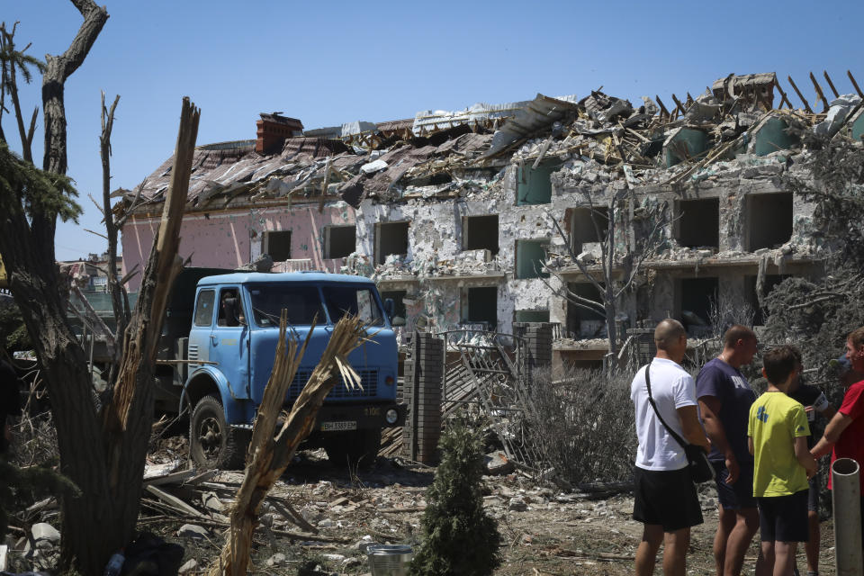 FILE - Local residents stand next to damaged residential building in the town of Serhiivka, located about 50 kilometers (31 miles) southwest of Odesa, Ukraine, July 1, 2022. While much of the attritional war in Ukraine’s east is hidden from sight, the brutality of Russian missile strikes in recent days on the mall in the central city of Kremenchuk and on residential buildings in the capital, Kyiv, were in full view to the world and especially to Western leaders gathered for a trio of summits in Europe. (AP Photo/Nina Lyashonok, File)