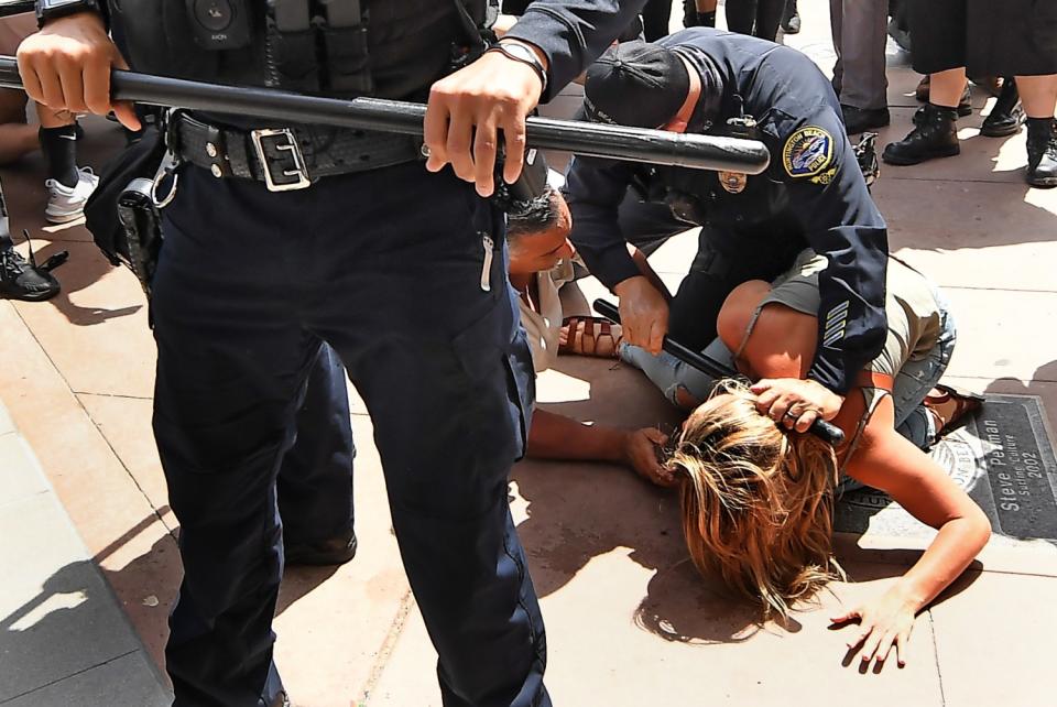 A Huntington Beach police officer grips a baton while trying to break up a scuffle between two people on the concrete