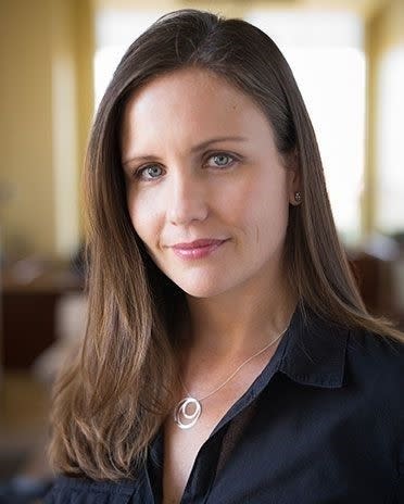 Woman in dark shirt with circular pendant, indoors, looking at camera