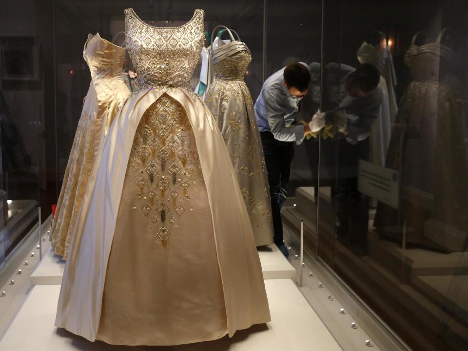 An employee cleans the glass cabinet displaying dresses worn by Queen Elizabeth II.