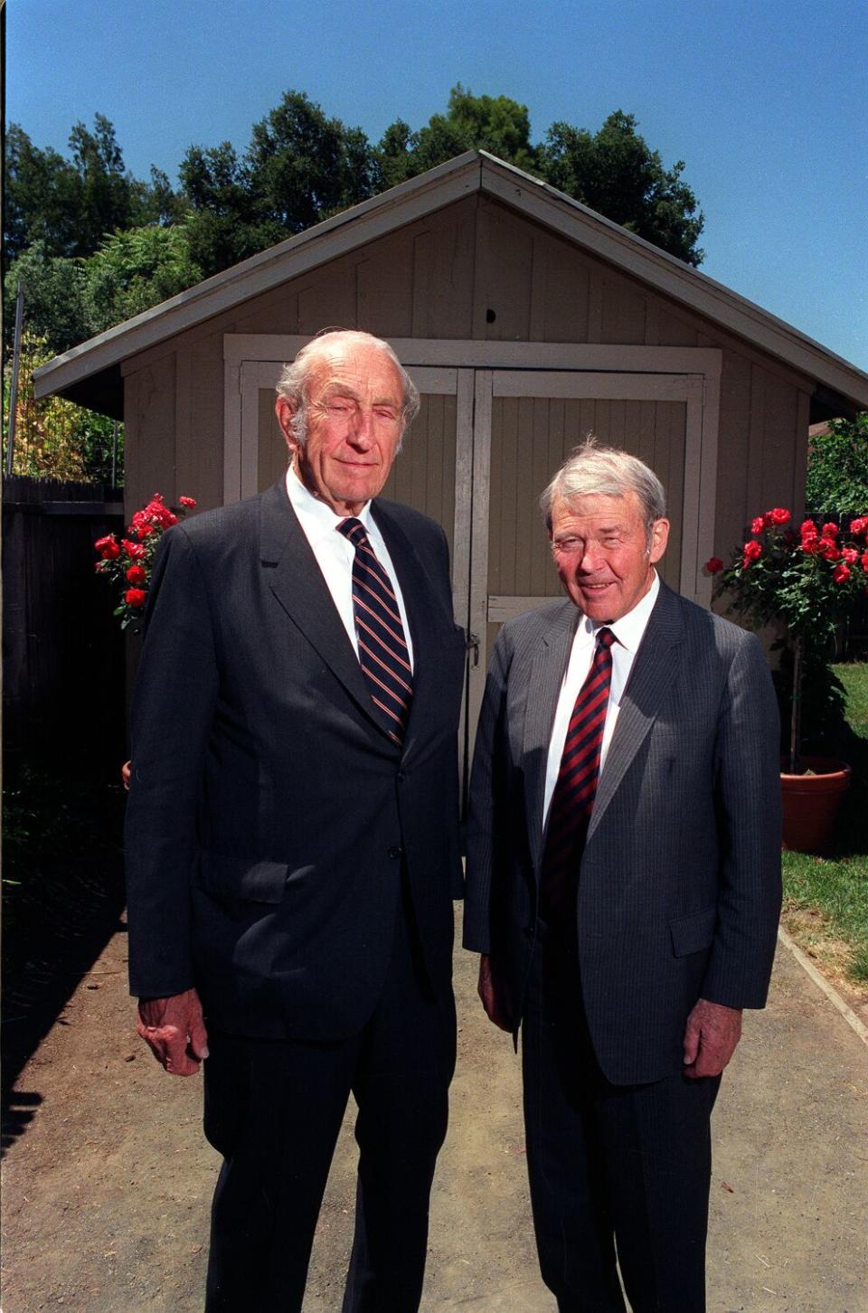 Two men stand in from of a garage.