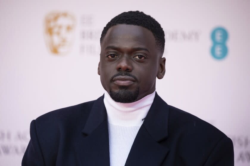 A man posing in a dark suit and white turtleneck