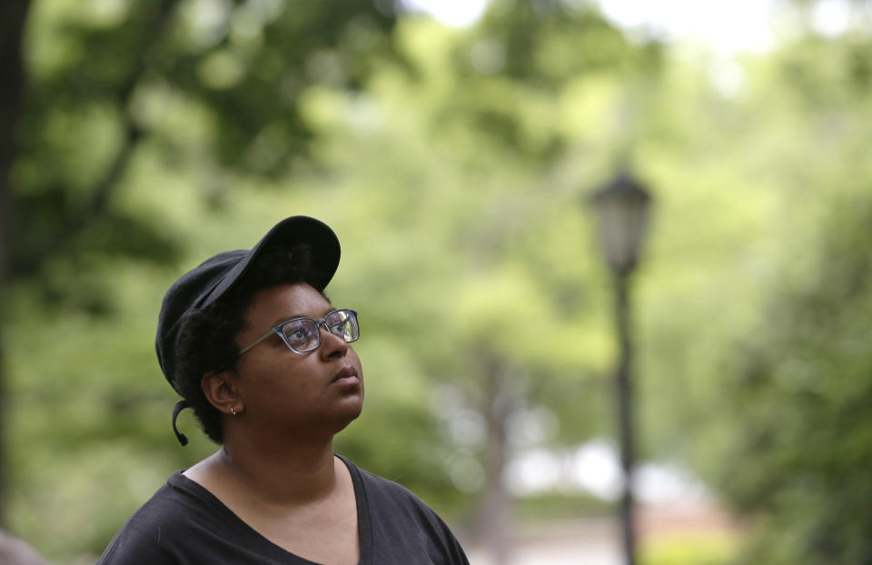In this May 15, 2018, photo, activist Maya Little glances upwards at the Confederate statue known as Silent Sam as she poses for a photo on campus at the University of North Carolina in Chapel Hill, N.C. Little, a UNC-Chapel Hill graduate student at the forefront of protests over a Confederate statue on campus, has been arrested again. News outlets report authorities say 26-year-old Maya Little is charged with inciting a riot and assaulting an officer during a rally Monday, Dec. 3. (AP Photo/Gerry Broome)