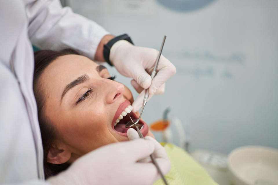 A woman is at the dentist's office, receiving a dental checkup from a dentist wearing gloves and using dental tools