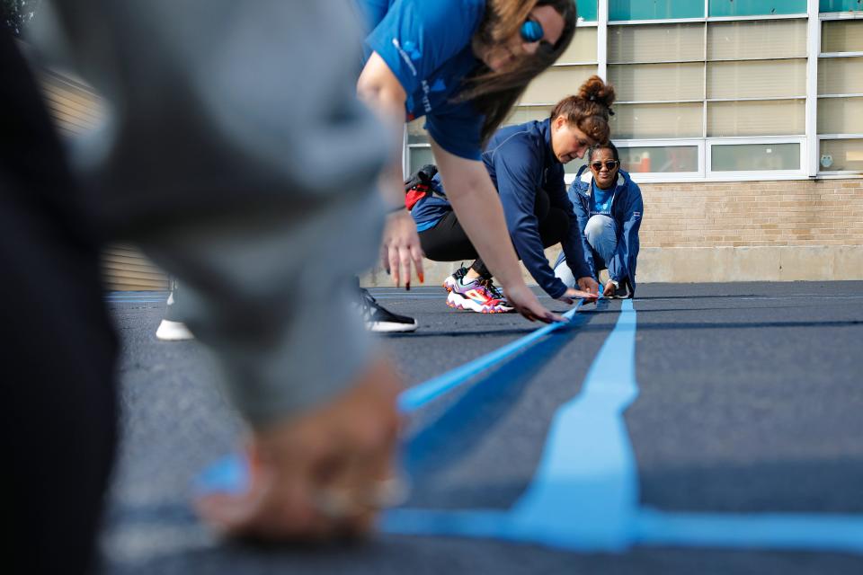 Blue Cross Blue Shield volunteers use tape before painting lines outlining a field for students to play tag at the Hathaway School in New Bedford.