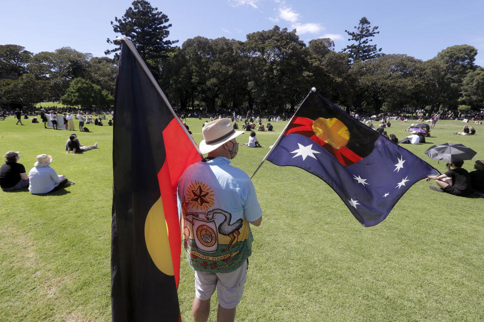 A man holds a modified Australian flag and the Aboriginal flag in a social distanced crowd during an Aboriginal-lead Invasion Day rally on Australia Day in Sydney, Tuesday, Jan. 26, 2021. Many of Australia's First Nations people say that sovereignty has never been ceded and oppose ongoing colonial violence and destruction. (AP Photo/Rick Rycroft)