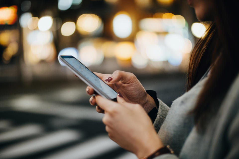 A close up of woman navigating location with smartphone in busy city street at night.