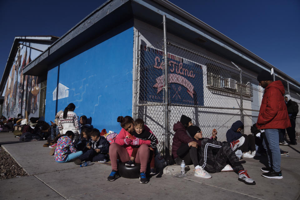 Migrants sit on the sidewalk outside a church.