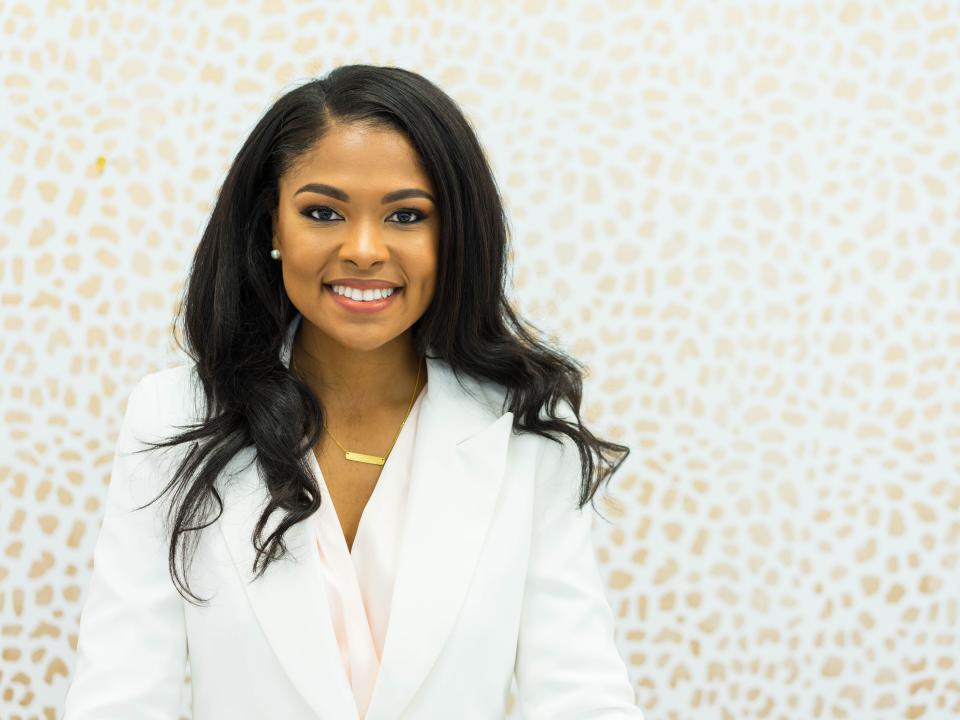 A woman wearing a white suit stands smiling at the camera