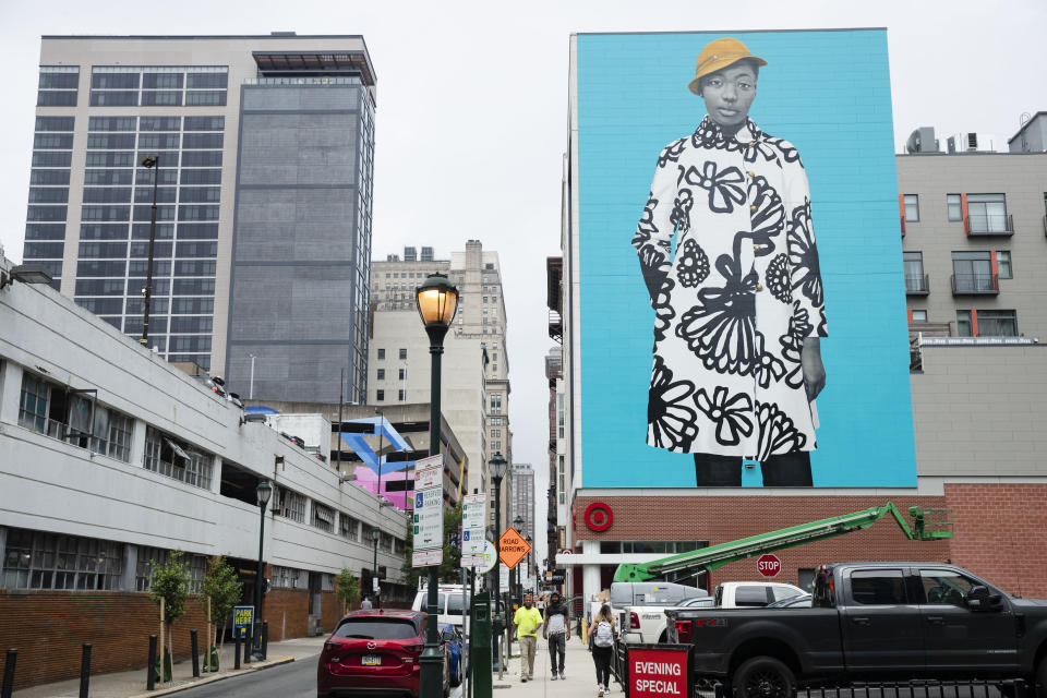 In this Tuesday, June 18, 2019 photo, pedestrians walk near a Mural Arts Philadelphia mural of Najee Spencer-Young by artist Amy Sherald by in Philadelphia. Sherald is the artist who painted the official portrait of Michelle Obama. (AP Photo/Matt Rourke)