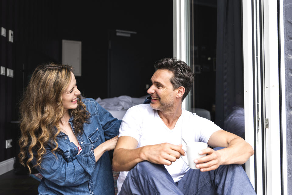 Happy couple in nightwear at home sitting at French window