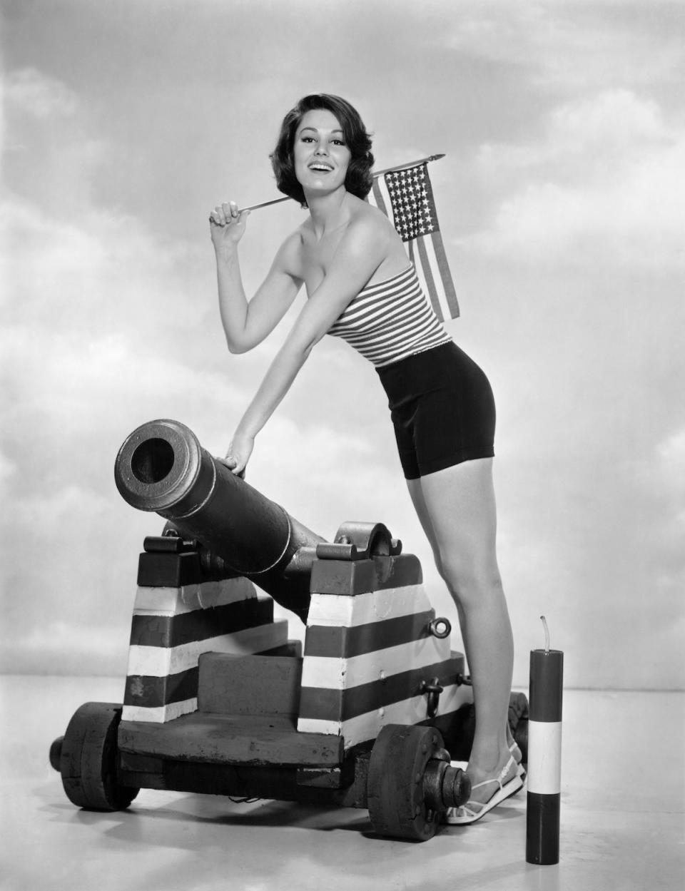 Paula Prentiss posing with a flag and cannon. 1962 vintage 4th of July