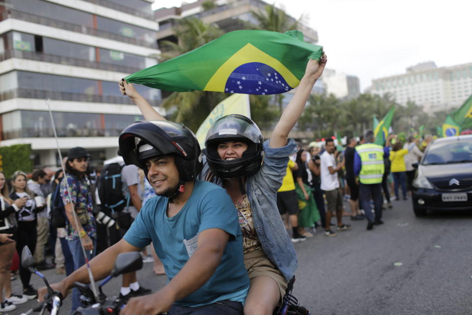 A supporter of presidential front-runner Jair Bolsonaro rides on the back of a motorcycle waving a national flag, outside Bolsonaro's residence in Rio de Janeiro, Brazil, Sunday, Oct. 28, 2018. Bolsonaro took a commanding lead in the race for Brazil's presidency, as voters apparently looked past warnings that the brash former army captain would erode democracy and embraced a chance for radical change after years of turmoil. (AP Photo/Silvia Izquierdo)