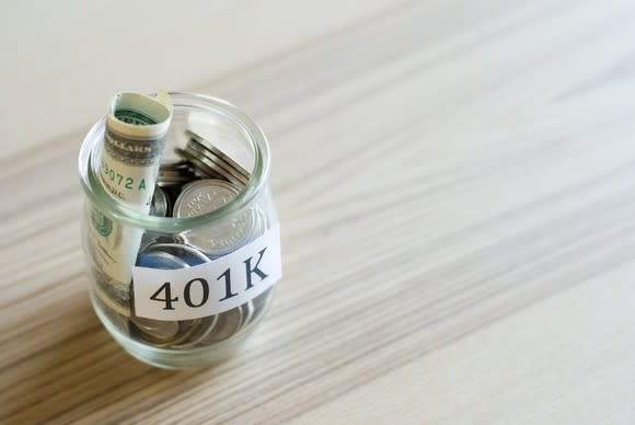 Glass jar labeled "401K" filled with rolled-up bills and coins.