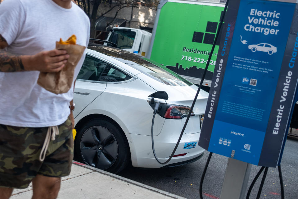 A person walks past a Tesla charging at a public PlugNYC electric vehicle charger  (Photo by Alexi Rosenfeld/Getty Images)