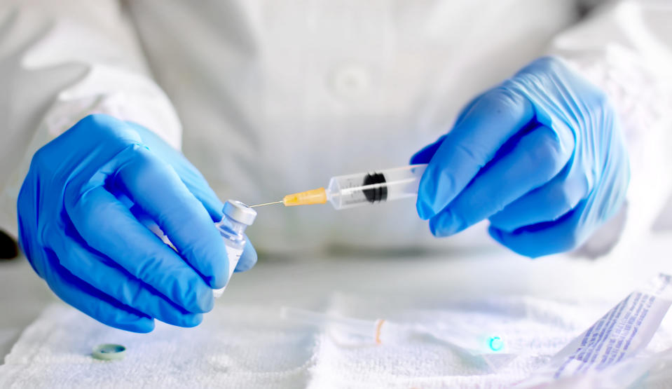 A person wearing blue medical gloves prepares an injection holding a vial and a syringe. 