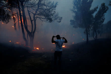 A man uses a cloth to protect himself from smoke as wildfire burns in the town of Rafina, near Athens, Greece, July 23, 2018. REUTERS/Costas Baltas