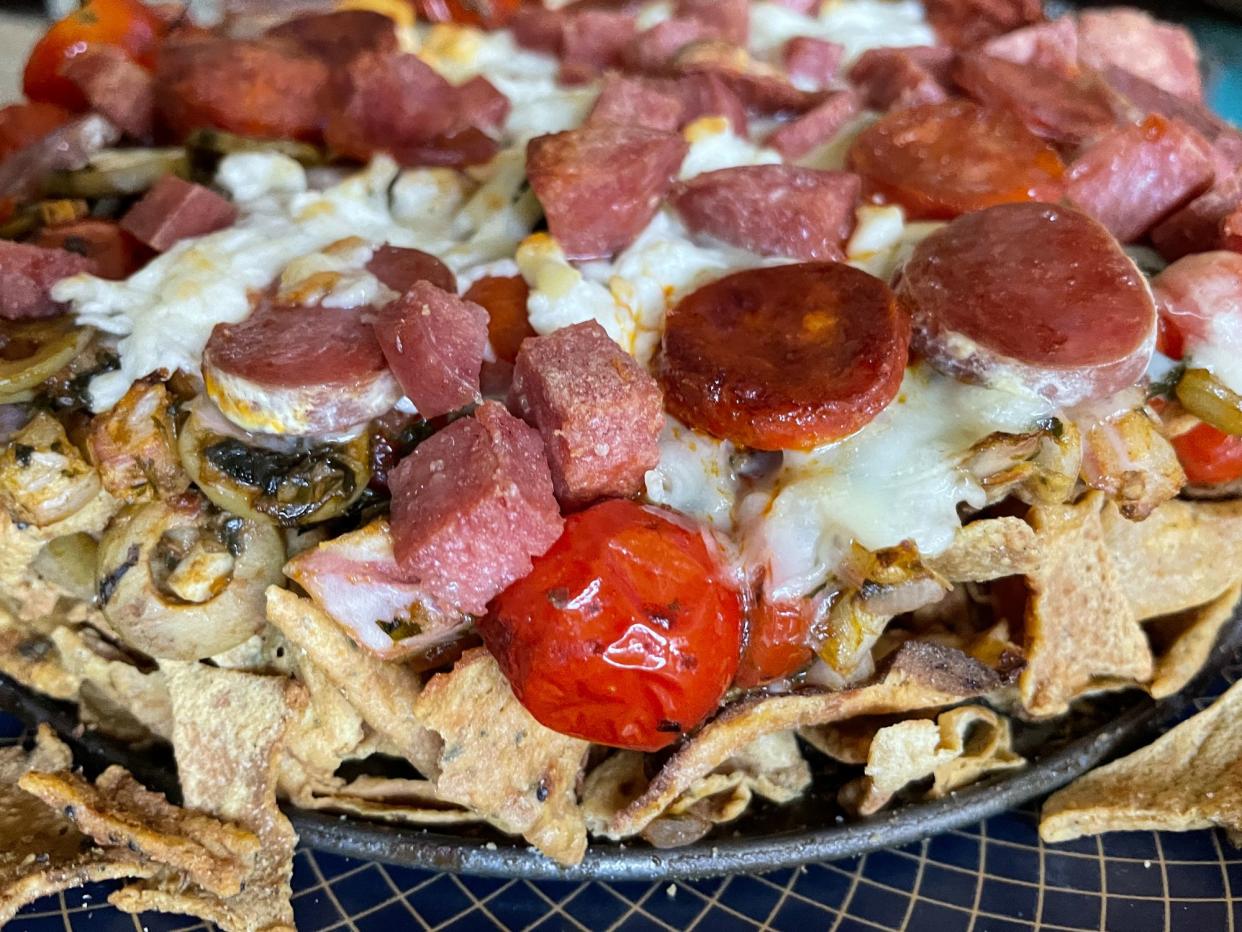 Stock photo showing close-up, elevated view of homemade loaded nachos recipe. This snack contains fresh, crunchy tortilla chips covered in melted cheese with cherry tomatoes, salami and Jalapeno peppers on a blue rimmed plate.