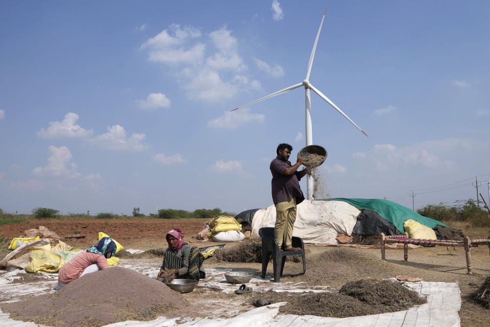 A family works in a field near a wind turbine, part of an Adani Group project, near Sadla village in Surendranagar district of Gujarat state, India, Monday, March 20, 2023. Gautam Adani and his companies lost tens of billions of dollars and the stock for his green energy companies have plummeted. Despite Adani's renewable energy targets accounting for 10% of India's clean energy goals, some analysts say Adani's woes won't likely hurt India's energy transition. (AP Photo/Ajit Solanki)