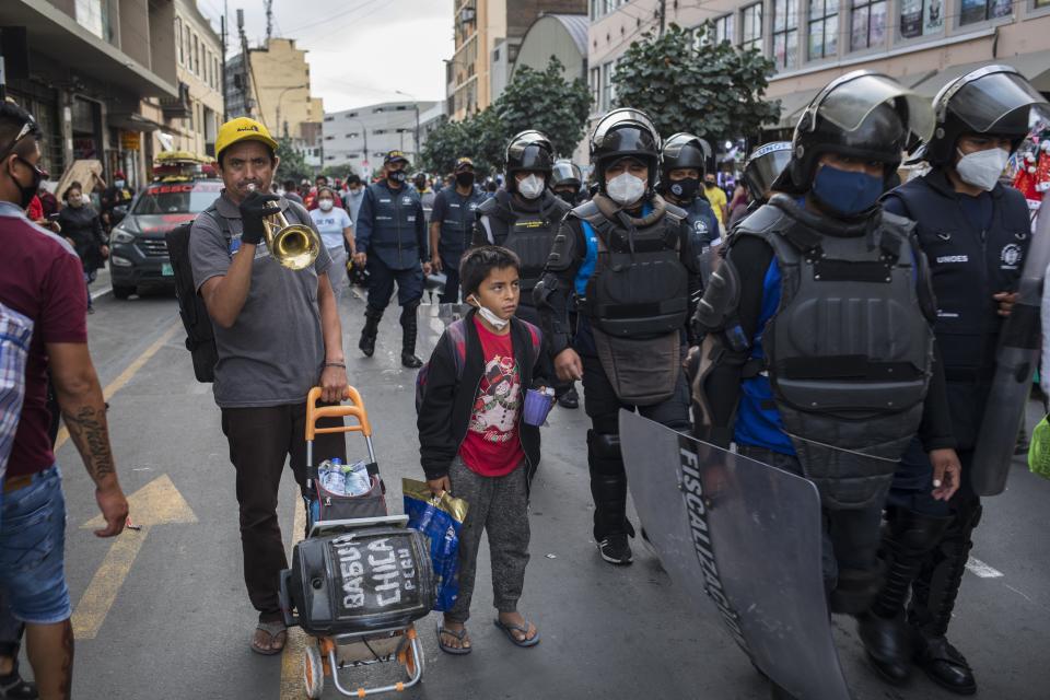 Wilder Alario Vazquez performs on the trumpet next to his son Wilfredo Moises at the Mesa Redonda Market, a popular spot for Christmas shopping, amid the COVID-19 pandemic in Lima, Peru, Monday, Dec. 21, 2020. (AP Photo/Rodrigo Abd)