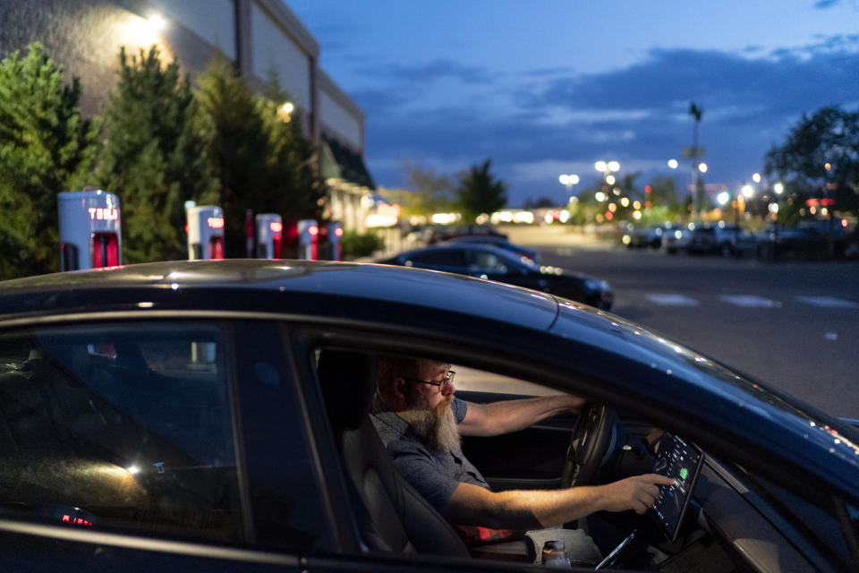 Mark Carlson recharges his Tesla electric vehicle during a shift driving for Uber in Oakdale, Minn., Friday, Sept. 30, 2022. Carlson believes, deeply, that America doesn't need to be so bitterly divided. "Liberalism and conservatism aren't that far apart. You can be pro-American, pro-constitutional. You just want bigger government programs. I want less." "We can work together," he says. "We don't have to, like, hate each other." (AP Photo/David Goldman)