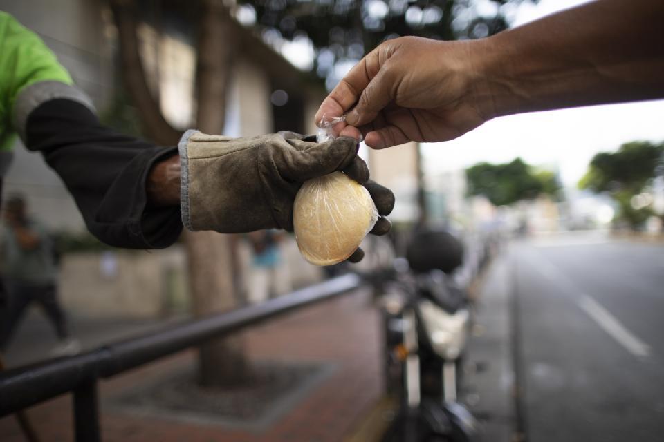 Una persona recibe un paquete de arepas caseras o empanadas de harina de maíz de Andrés Burgos, un publicista de 55 años, en Caracas, Venezuela, el miércoles 21 de octubre de 2020. (AP Foto/Ariana Cubillos)