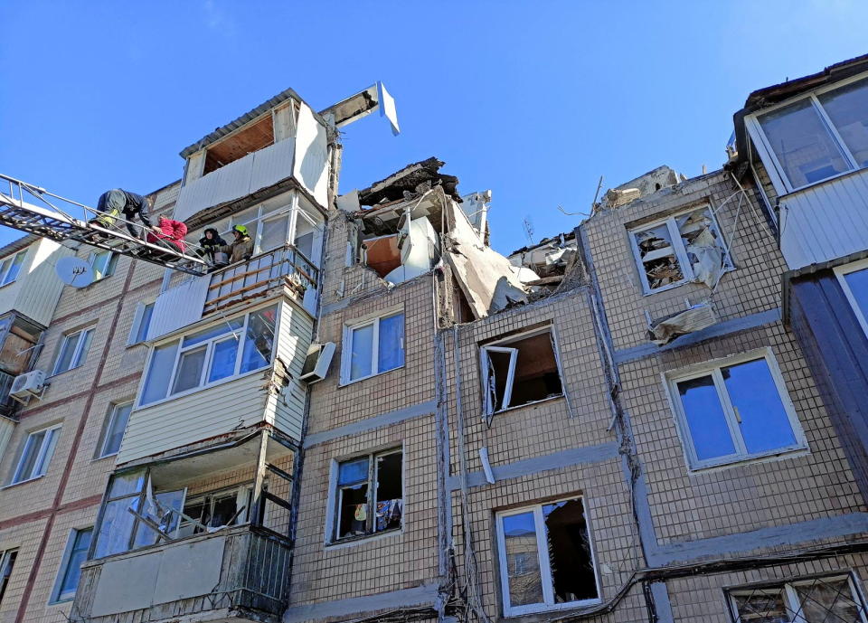 Using a ladder to the top floor of a shelled residential building, rescuers evacuate a woman.