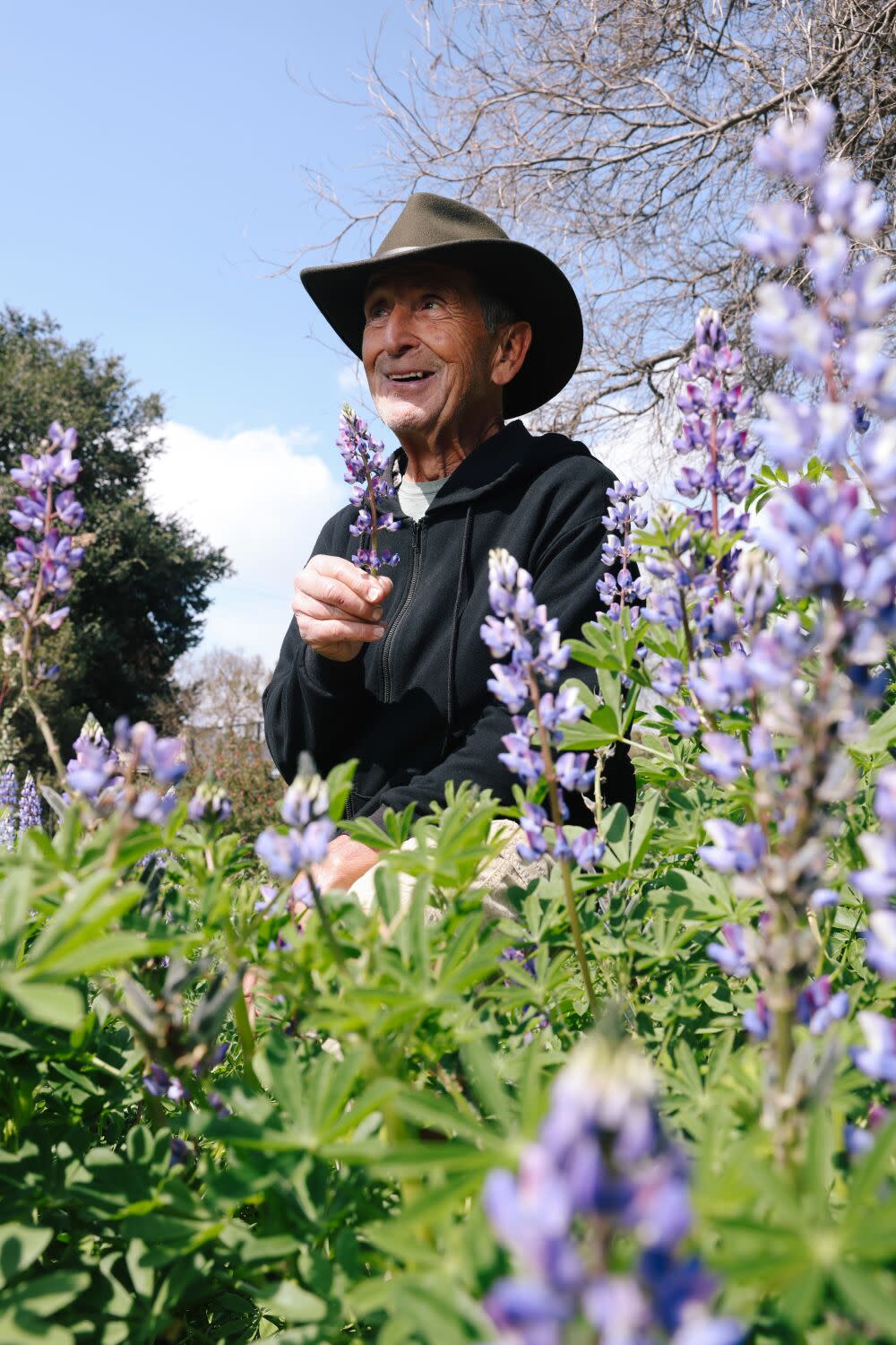 A man standing in a garden smiling and holding a flower in his hand