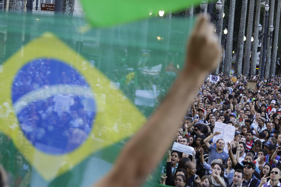 <p> A demonstrator holds up a Brazilian flag in front of a group of protestors gathered in the main plaza of Sao Paulo, Brazil, Tuesday, June 18, 2013. Some of the biggest demonstrations since the end of Brazil's 1964-85 dictatorship have broke out across this continent-sized country, uniting multitudes frustrated by poor transportation, health services, education and security despite a heavy tax burden. (AP Photo/Nelson Antoine)</p>