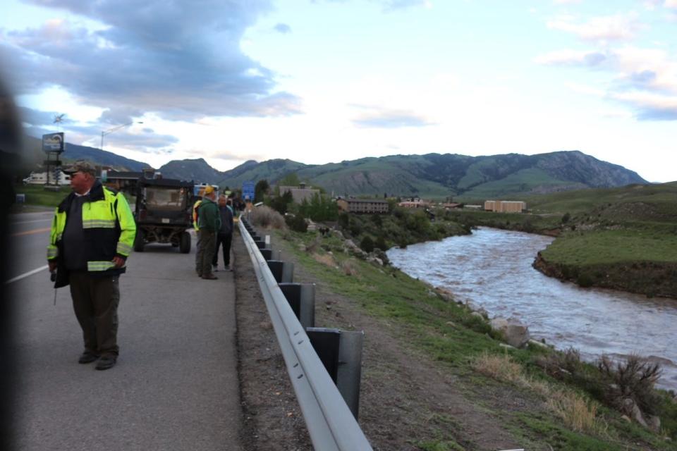 Onlookers and an EMT gather along the side of the road after a bunkhouse was swept away into the Yellowstone River.