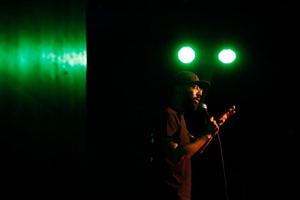 Man in hat and glasses standing onstage with a mic