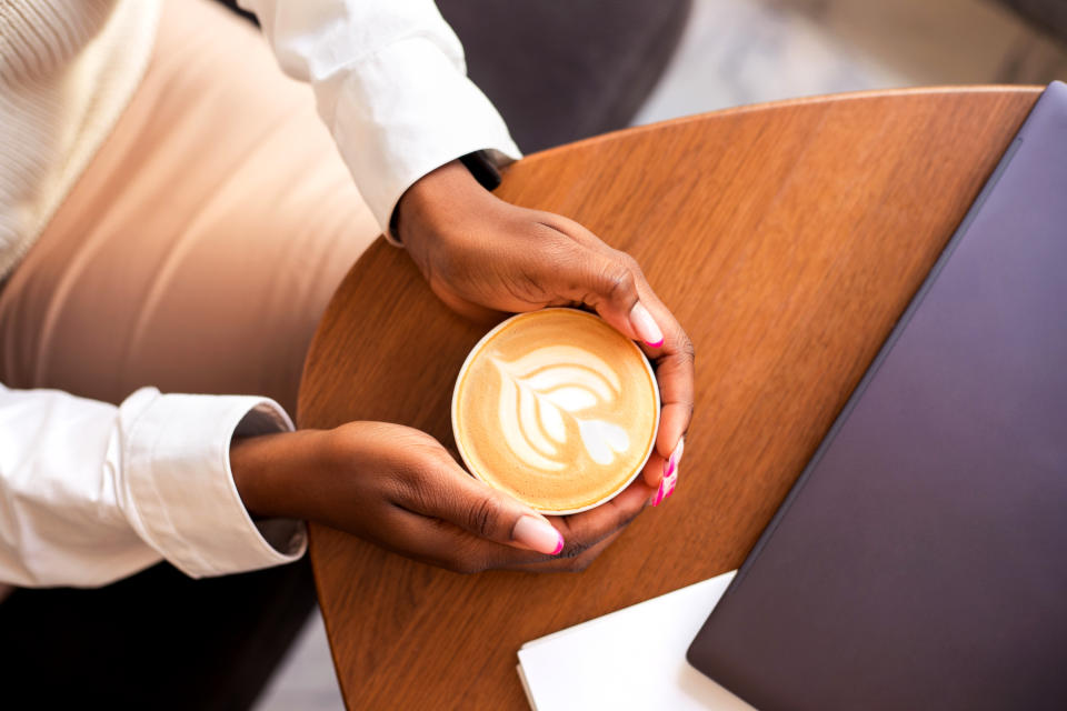 Woman holding a cup of coffee on a wooden table.