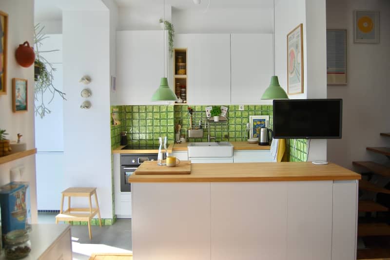 A view of the kitchen area with a green backsplash and white cabinets.