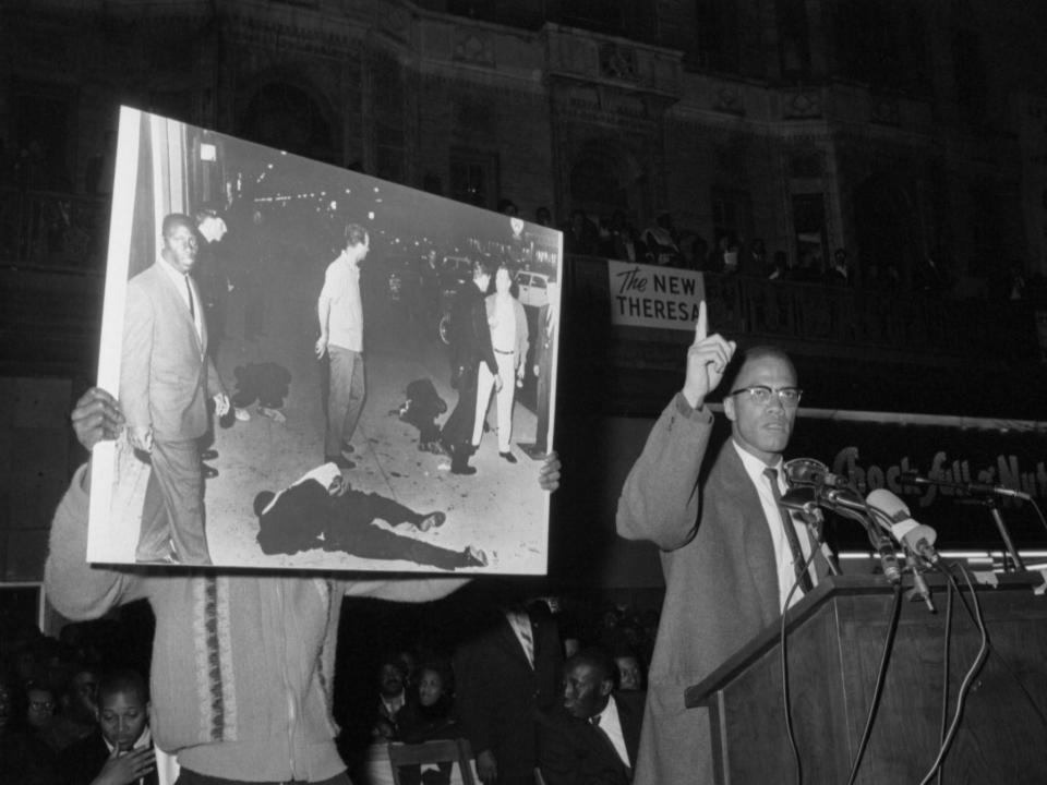 Black Muslim minister Malcolm X has assistant hold picture of fallen black men as he addresses a Harlem rally in support of integration efforts in Birmingham in 1963.
