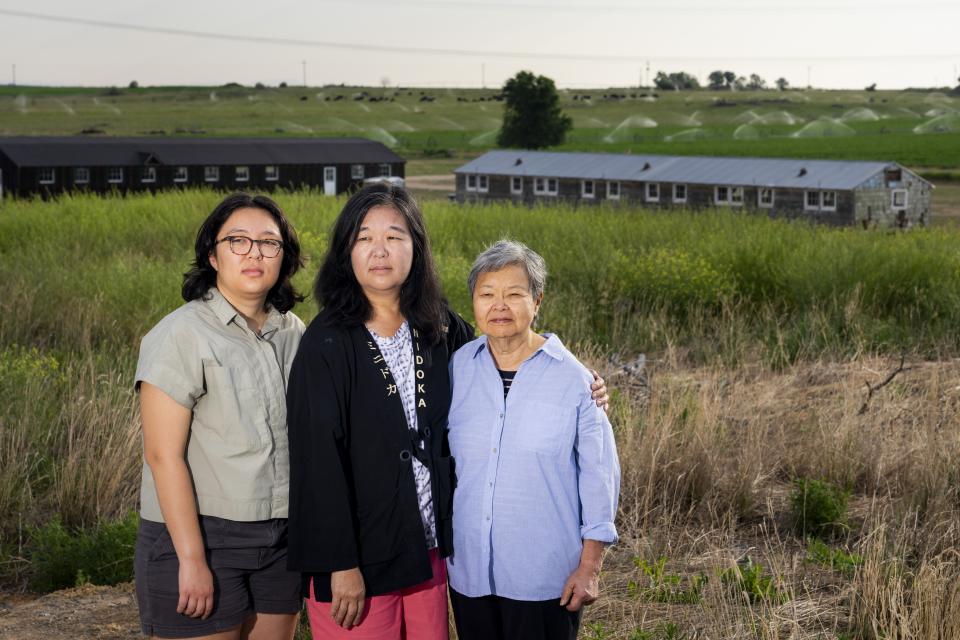 Minidoka survivor Mary Tanaka Abo, 83, at right, poses for a portrait with daughter Julie Abo, center, and granddaughter Maya Abo Dominguez, left, in front of a historic mess hall and barracks at the Minidoka National Historic Site, Saturday, July 9, 2023, in Jerome, Idaho. Tanaka Abo says she didn't want Julie or Maya to feel the same sense of shame surrounding incarceration as she did. Instead, she chose to speak openly about her experience with her daughter and granddaughter, and has attended multiple pilgrimages with her family. (AP Photo/Lindsey Wasson)