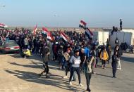 Iraqi demonstrators carry Iraqi flags as they block the road during ongoing anti-government protests in the outskirts of Nassiriya