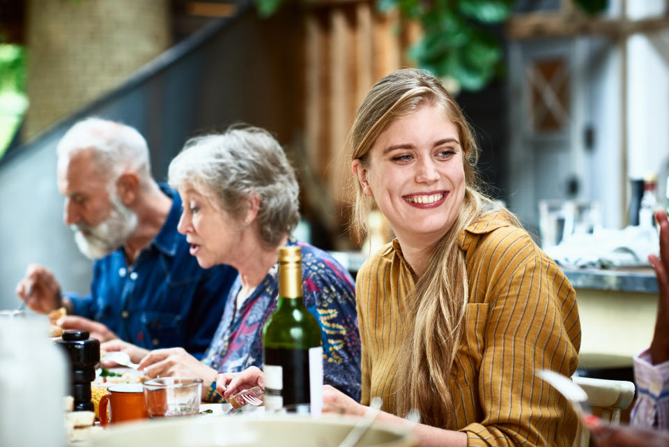 Cheerful woman in her 30s with long blond hair sitting with friends, socialising, eating with friends at home