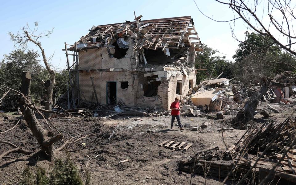 A resident walks past a crater and a destroyed house after a missile strike in Kyiv