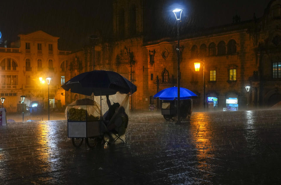 Vendedores callejeros se resguardan de la lluvia ante la basílica de San Francisco, en La Paz, Bolivia, el 25 de enero de 2024. (AP Foto/Juan Karita)