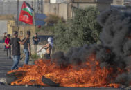 Palestinian protesters burn tires and use slingshots during clashes with Israeli soldiers at the entrance the Jewish settlement of Beit El, background, near the West Bank city of Ramallah, Tuesday, June. 15, 2021. (AP Photo/Nasser Nasser)