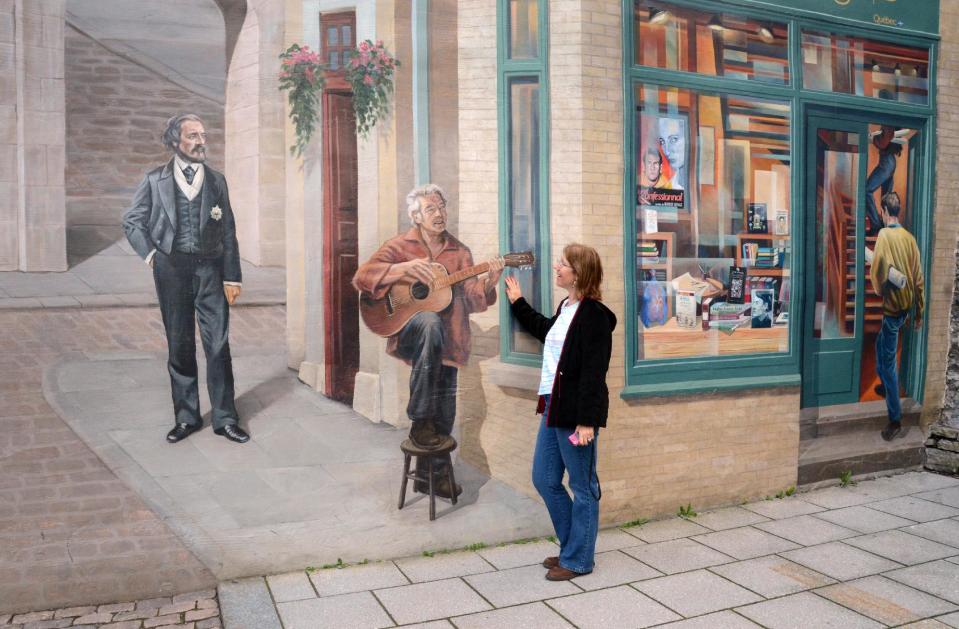 In this photo taken Aug. 13, 2013, a visitor admires a mural, covering the side of a building in Quebec City. For many cyclists, Quebec City is a starting point for a multi-day ride along the St. Lawrence River on Route Verte 1. (AP Photo/Calvin Woodward)