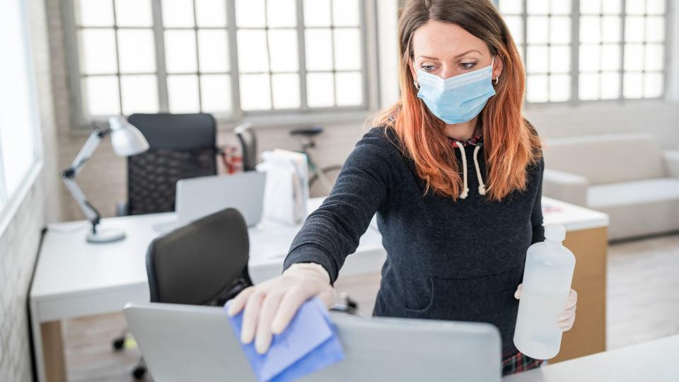 Woman in the office using disinfectant  for sanitizing monitor surface during COVID-19 pandemic.