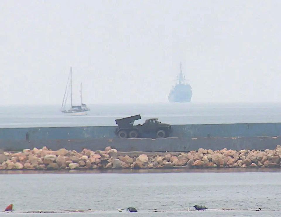 The BM-21, or variant thereof, positioned along the seawall at the mouth of Sevastopol Bay. A section of a floating boom strung across the entrance to the harbor can be seen at the bottom of the picture. What the Russian Navy's Black Sea Fleet said was the Project 18280 <em>Yuriy Ivanov </em>class intelligence ship <em>Ivan Khurs</em> returning to port after the recent drone boat attack is seen at the top right. <em>Russian Navy Black Sea Fleet</em>